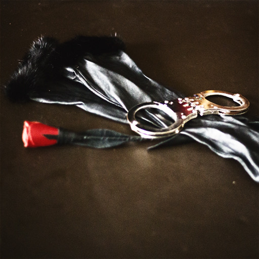 Rote Rose, schwarze Seide und Handschellen auf dunklem Grund